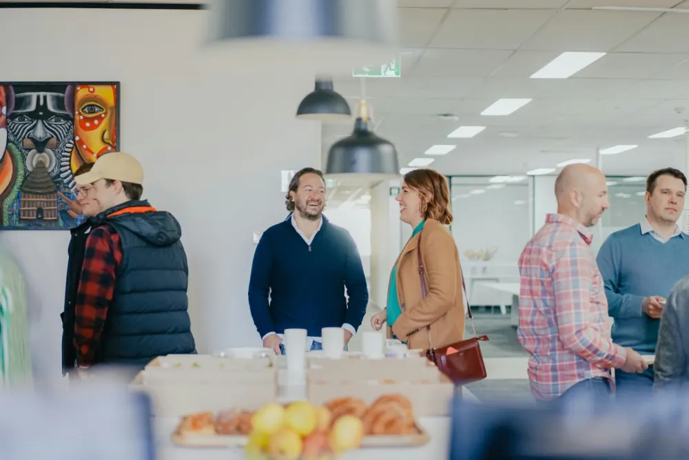 Mehrere Menschen stehen im Gespräch an einem Tisch mit Kaffee und Gebäck.