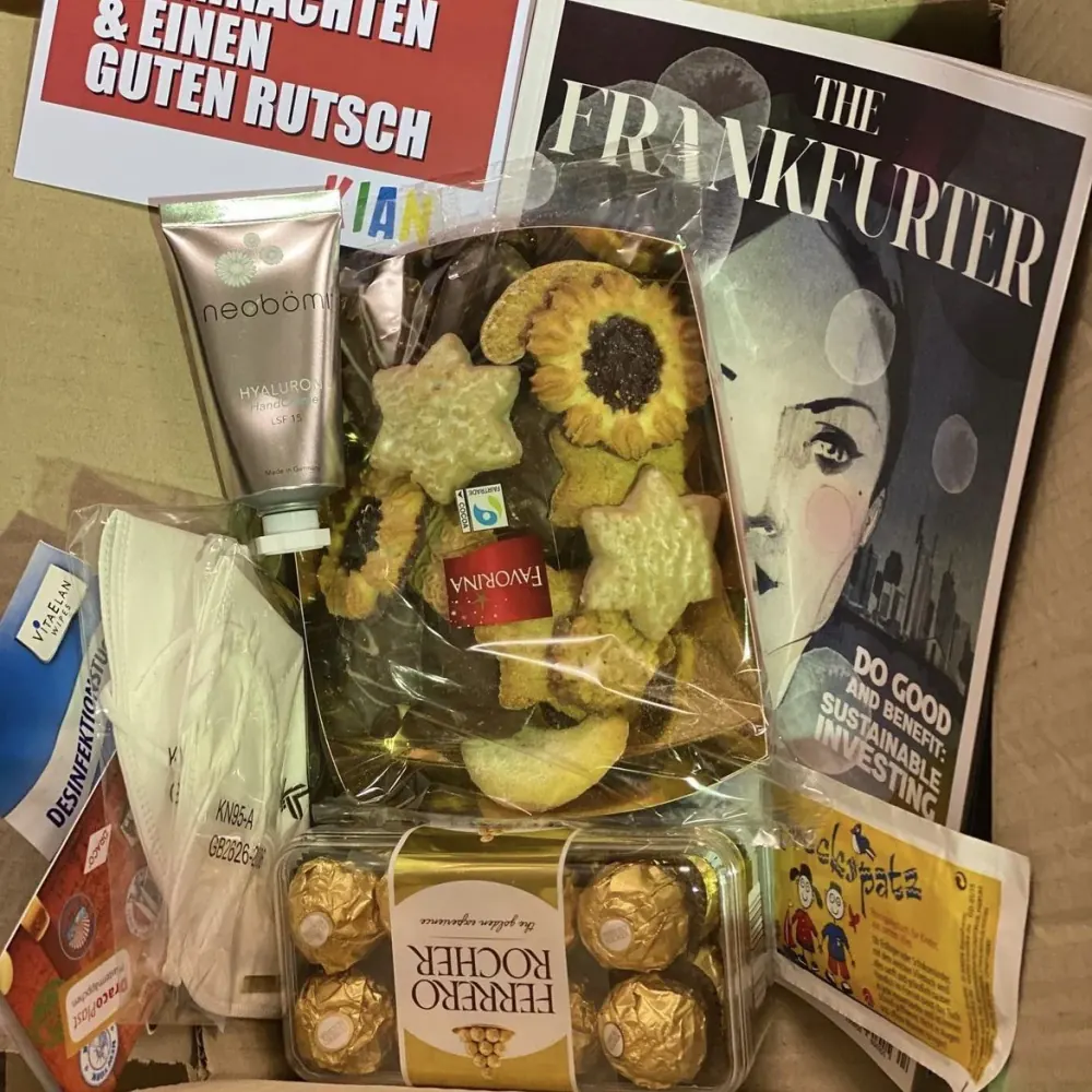 Ein geöffneter Karton des Christmas Kits mit Plätzchen, Handcreme, Masken, Desinfektionstüchern, Pralinen und einer Weihnachtskarte.